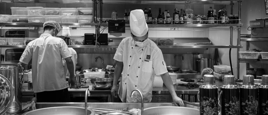 Ontario food safety inspector reviewing certification paperwork in a commercial kitchen environment, with food handlers and managers present